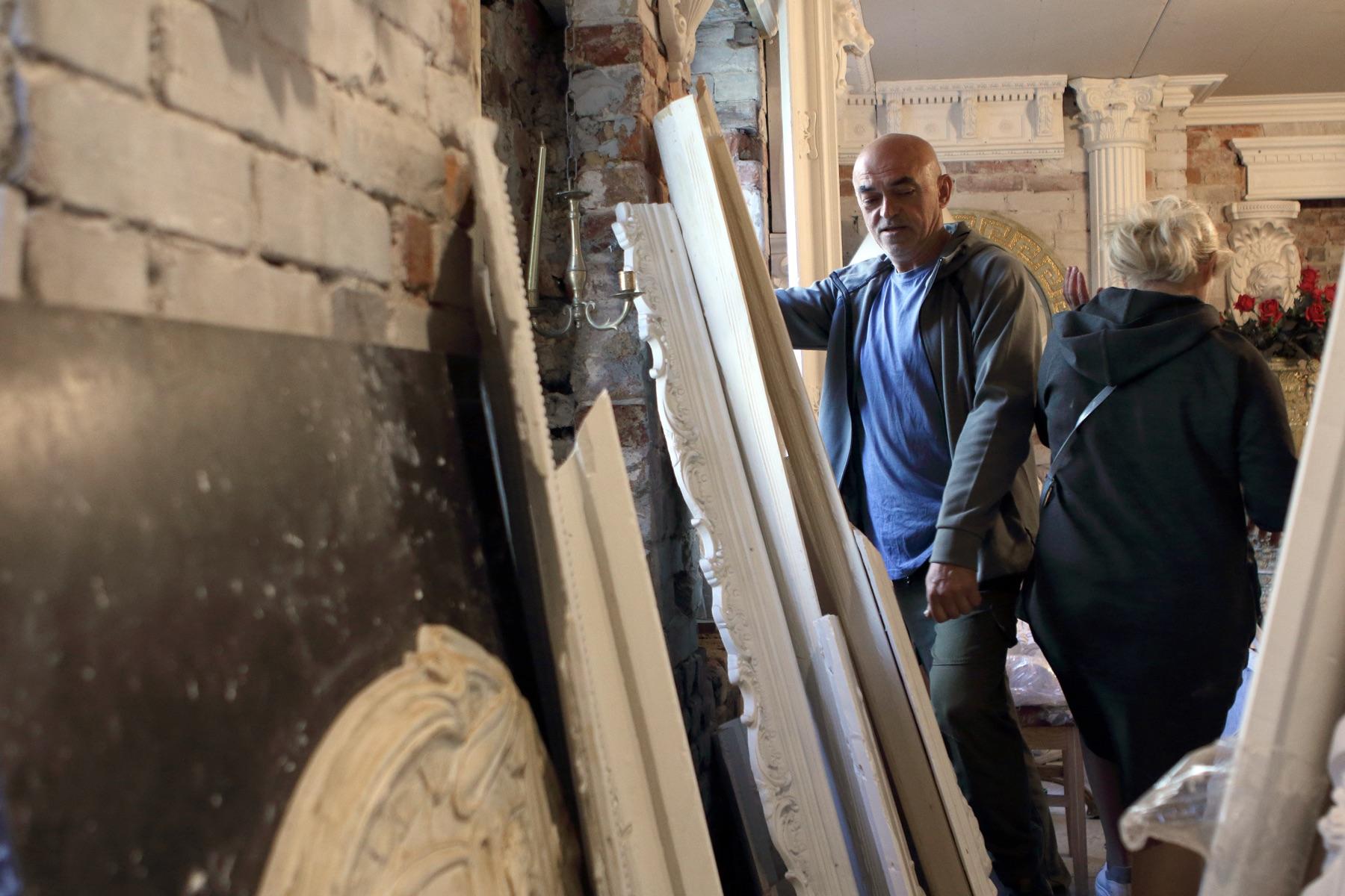 Master sorts white plaster cornices and panels leant against a brick wall