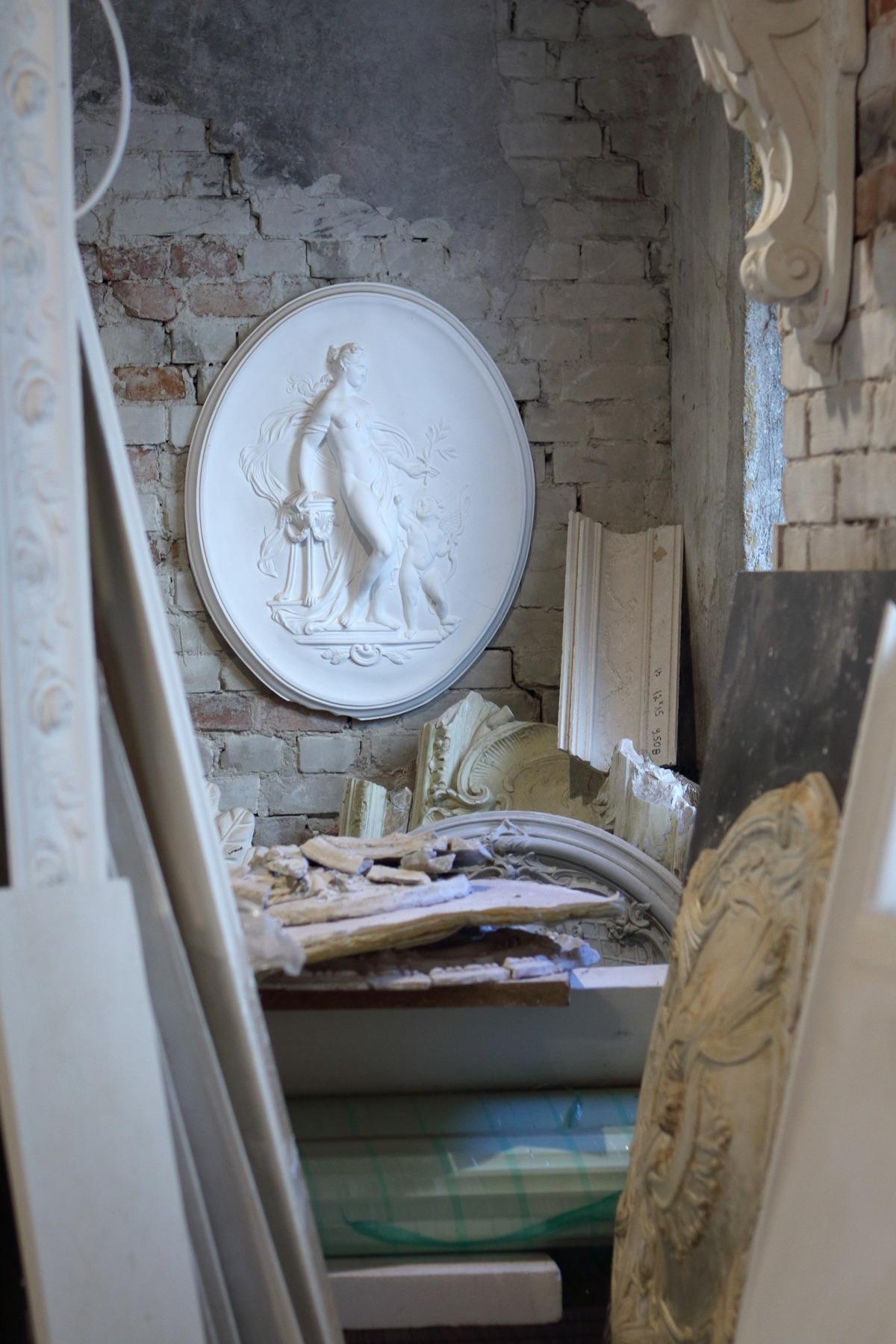 Oval plaster medallion with female figure on a brick wall in the workshop