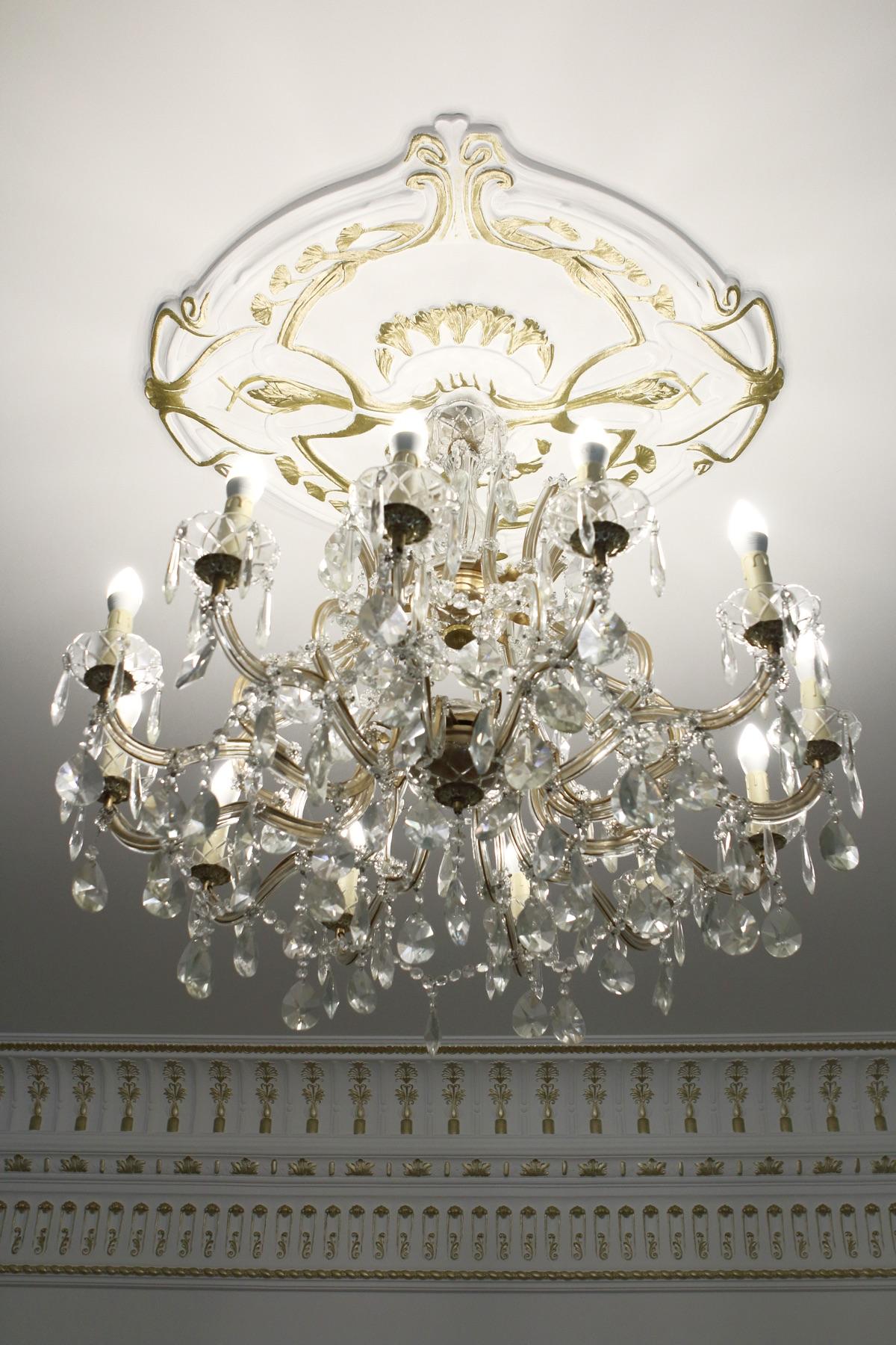 Figured ceiling rosette with gold ribbon ornament and a multi-arm crystal chandelier beneath